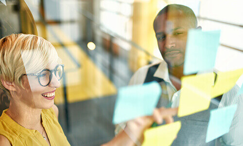 Two people working with sticky notes on wall